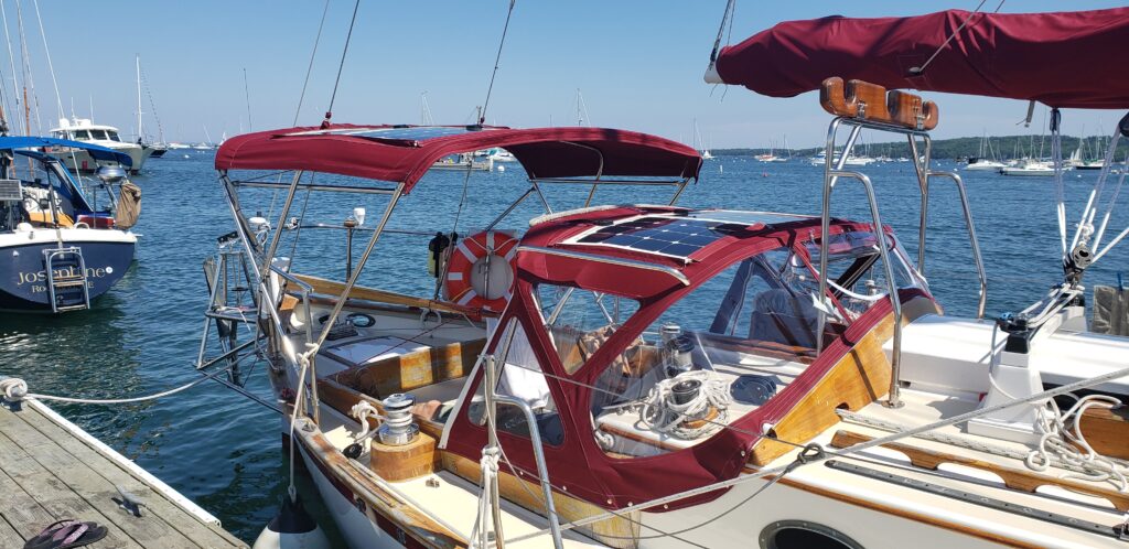 Deep red dodger and bimini, both with soft solar panels. Matching sail cover on boom. 